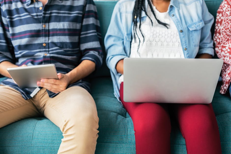 Image of three people sitting on a green couch, holding laptops and paper in their hands