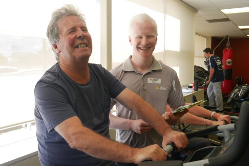 John riding on the exercise bike with Kane in the background watching over 