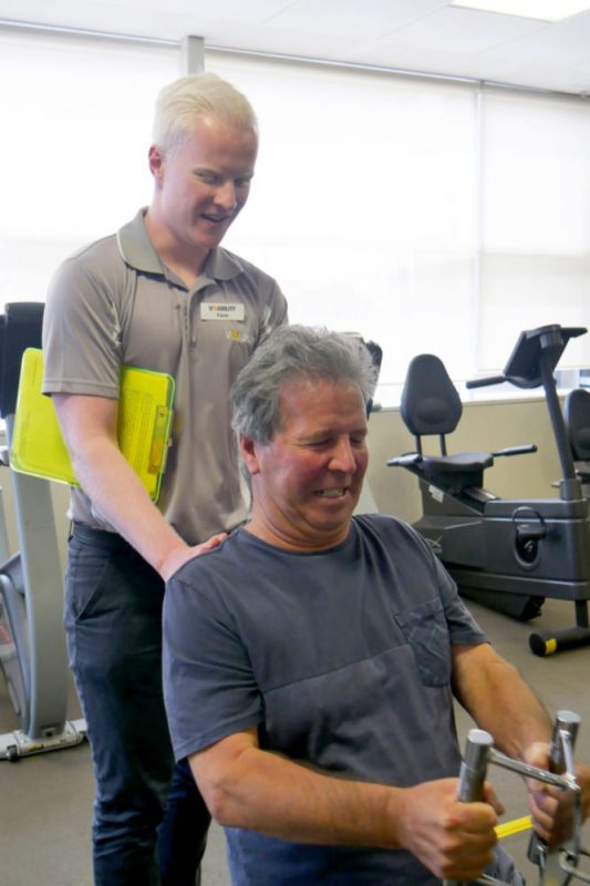 Kane holds the top of John's back as he works on weights 
