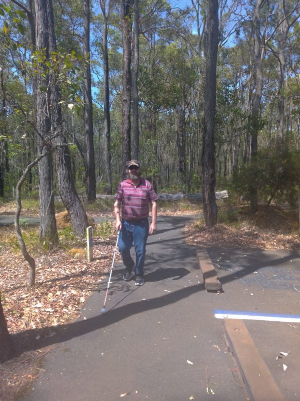 Phil walks along a forested area holding his white cane