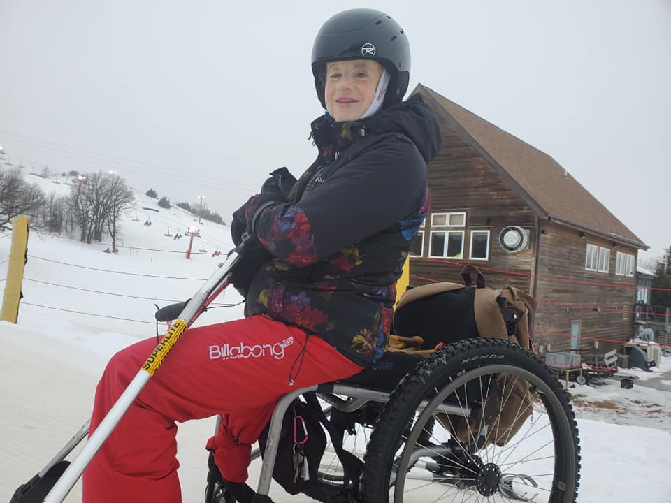 Kylie on slope in her all terrain wheelchair smiling holding outriggers