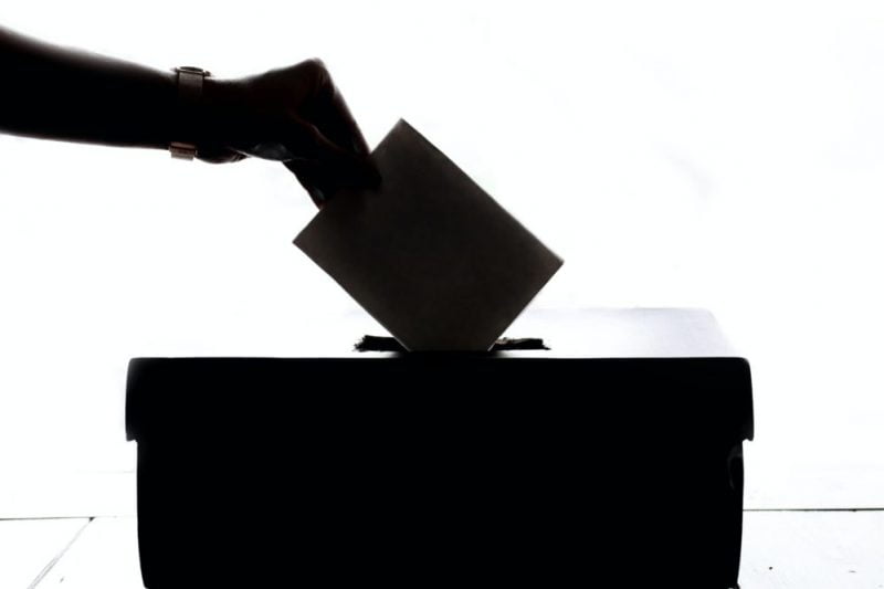 Image shows hand dropping a ballot in ballot box