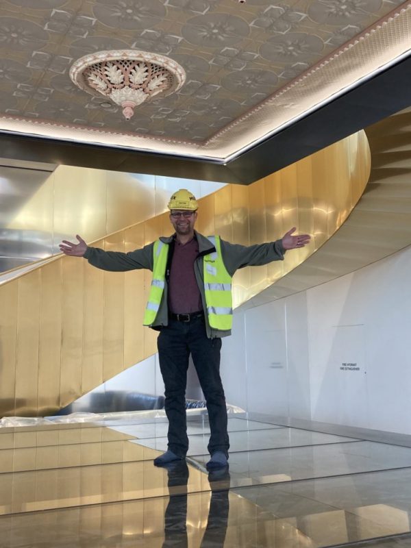 David in flourescent jacket and hard hat stands on top of a glass structure overlooking the heritage buildings