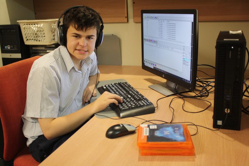 Thomas wearing headphones sits in front of a computer screen. His fingers are on a keyboard