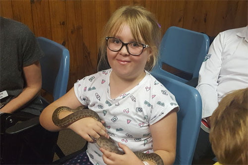 A girl attending the Fun Club holds a snake in her forearms