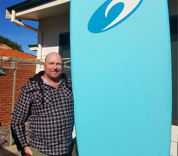 Todd standing next to upright blue surfboard