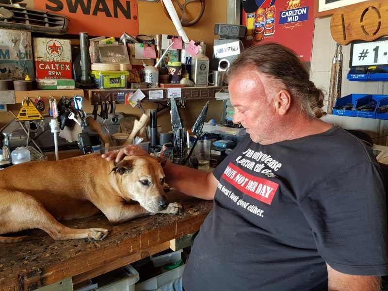 Barry sitting next to his bench and stroking his pet dog