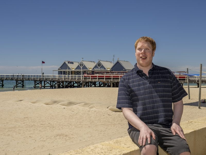 Graham sitting in front of the famous Busselton Pier next to the beach