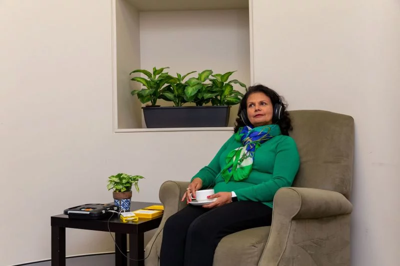 Woman sits on sofa in lounge listening to a talking book. She has headphones on her head. VisAbility will have a new parent name of EverAbility