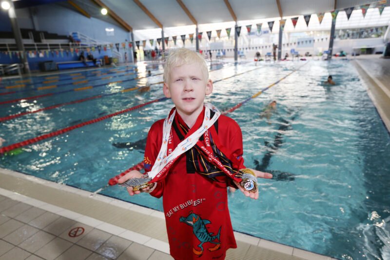 Kaleb in swimming pool holding up his medals