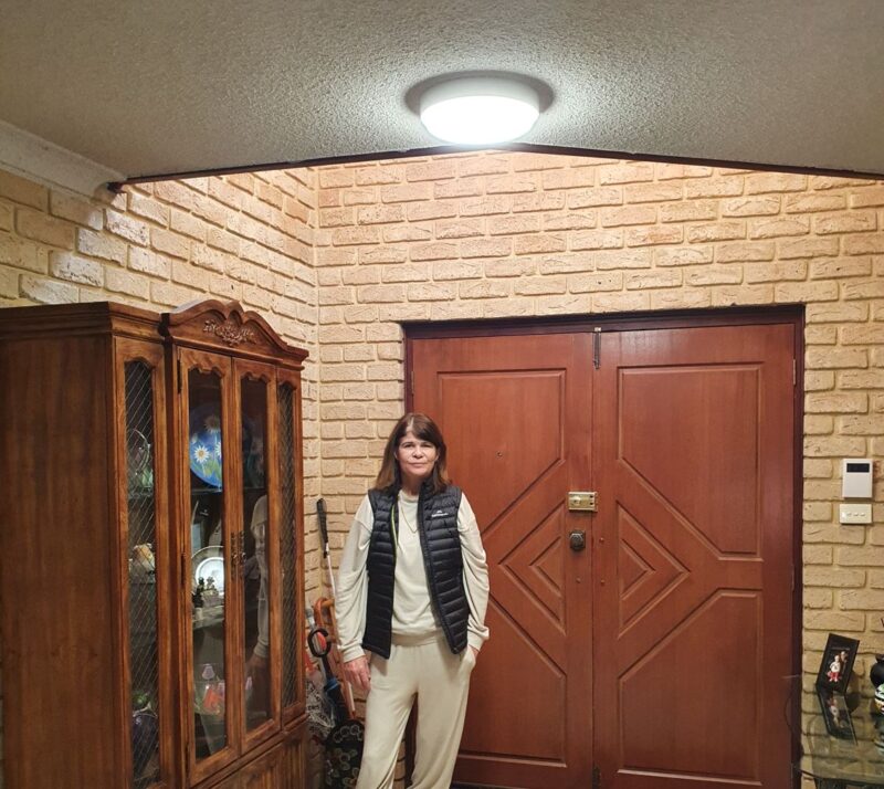 Anne stands at the entrance door of her home with bright light in front