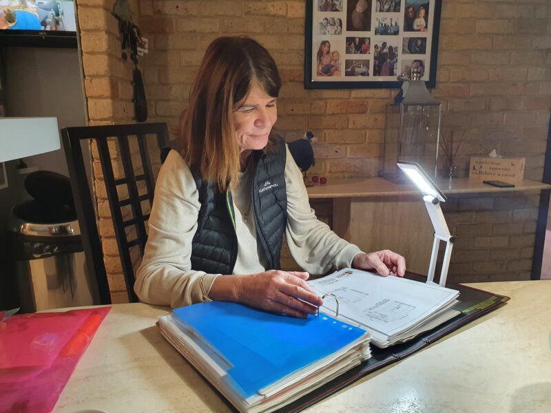 Anne reads a binder full of paperwork with the portable spotlight shing downwards