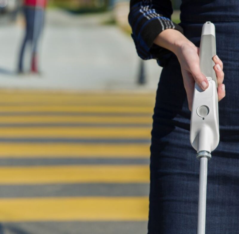 Person crossing the road holding a WeWALK device