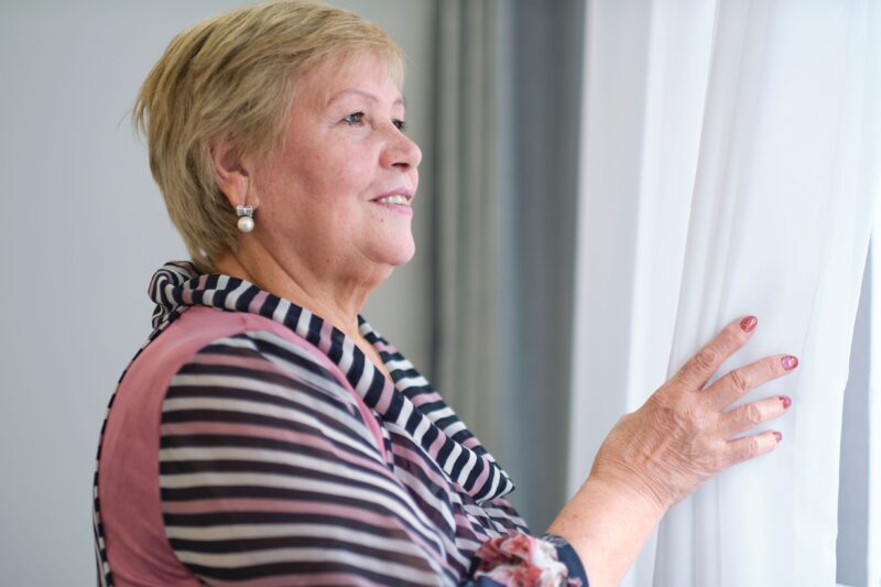 Older woman pulling back blinds