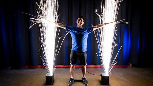 Man stands with arms outstretched between two vertical columns of sparks