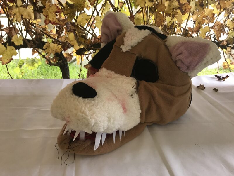 Big wolf like mask with brown and white felt and big nose on wire frame on table