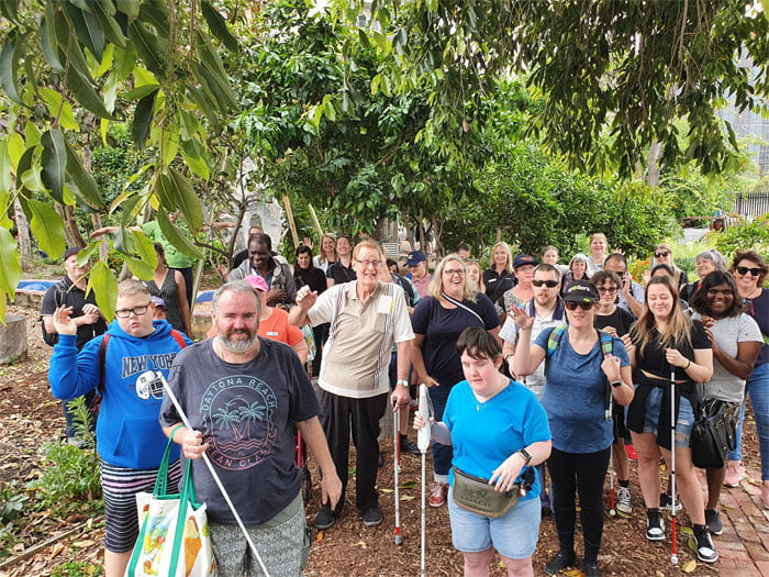 A large group of people with white canes pose and smile for the camera at Perth City Farm
