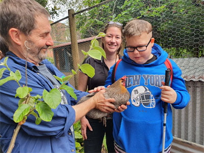 A man holds a chicken while a woman and young man look on