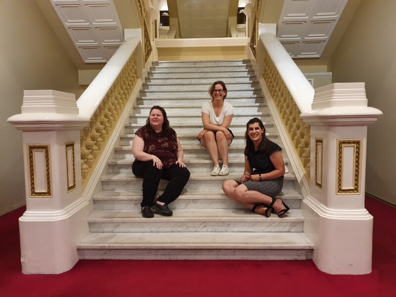 Grace, Kat and Zel sit on the steps of His Majesty's Theatre Perth