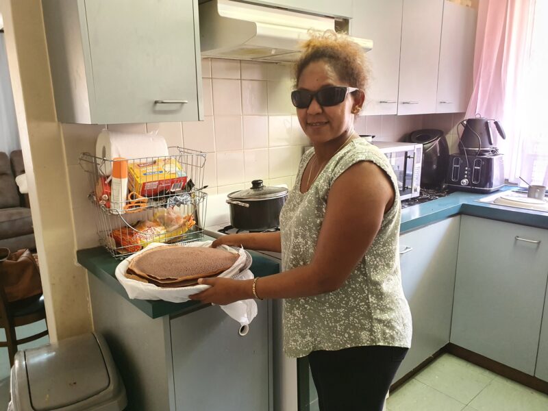 Saba in her kitchen holding a plate full if traditional Eritrean pancakes 