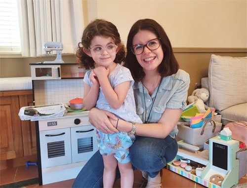 Madeleine and mum Simone smile at the camera with a toy cooker in the background