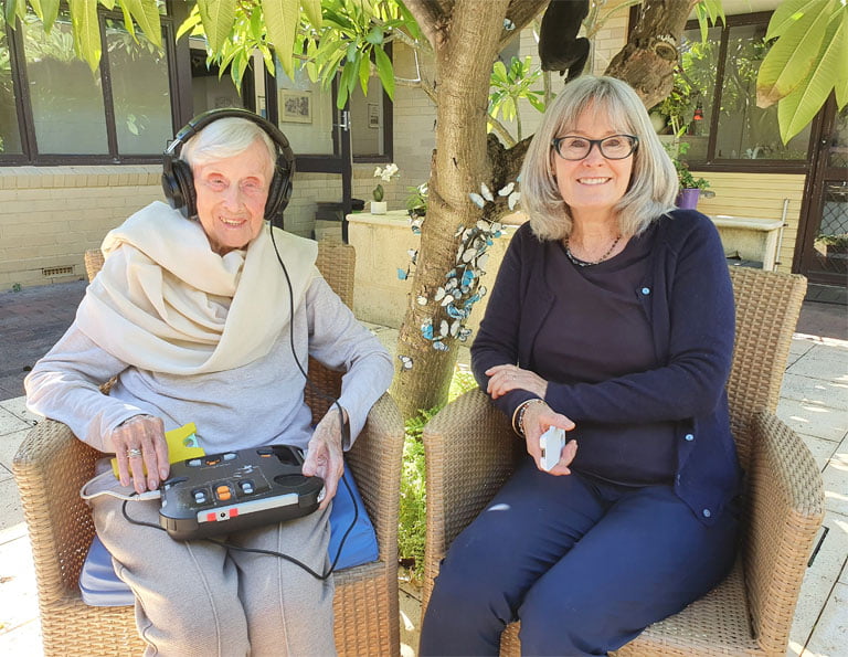 Gwen sits next to her daughter Alison with the audio player on her lap and a cartridge in her hand