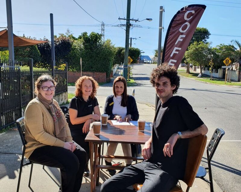 A group of people sit around a table in outdoor space outside a café 