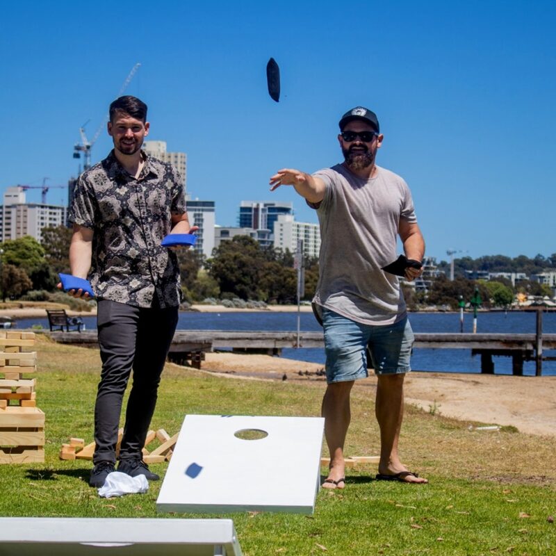 Two people throw bags into hoops with backdrop of Perth in rear 