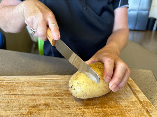 Woman holds non-sharp knife that is touching a potato 