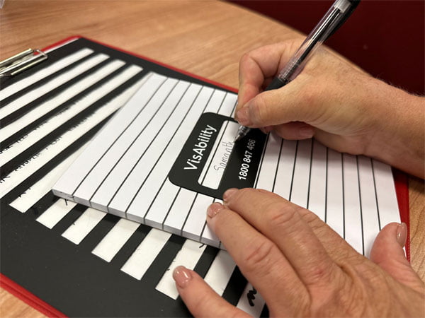 Woman writes within a signature guide on a pad. Larger A4 signature guide is in the background.