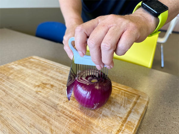 A hand is placed on a red onion with the onion holder's prongs piercing the onion itself