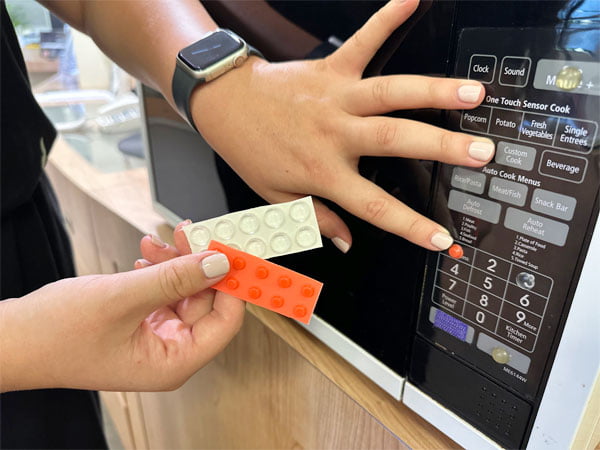 Hand is placed close to orange tactile bump situated on microwave with the other hand showing tactile bumps