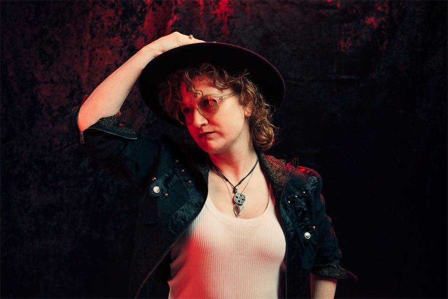 Simone stands in darkened room with a large hat and nodding to one side