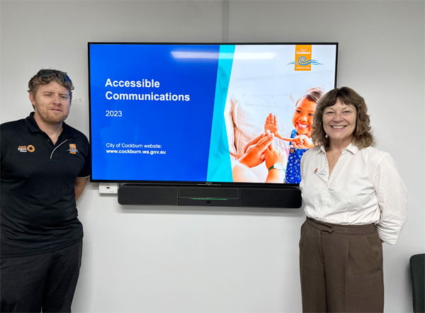 Ben and Samantha stand by a screen which says Accessible Communications 2023