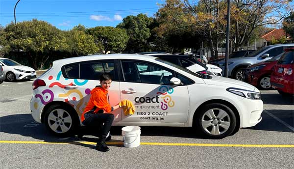 Marcus crouches next to the CoAct VisAbility car with a cloth and bucket 