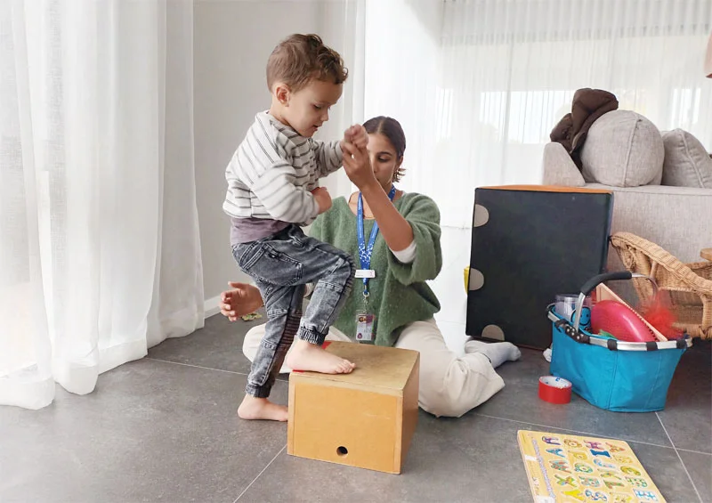 Child steps onto a wooden block with Physiotherapist holding the child's hand.