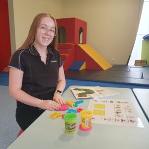 Emily sitting at a child's desk playing with playdough and other kindy activities