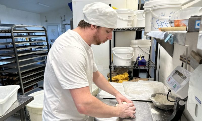 Rhys in the bakery kneading dough on the benchtop.