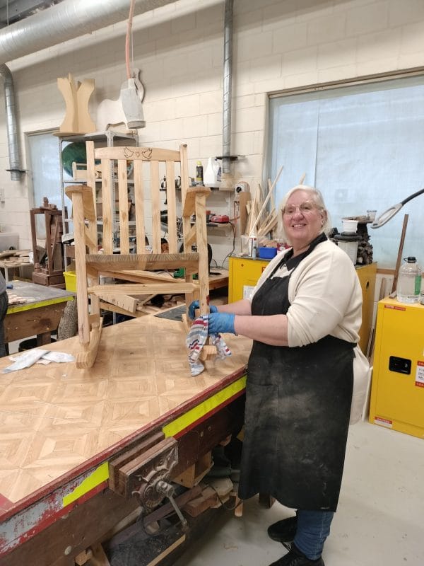 A CAC member standing by the wooden rocking chair they built