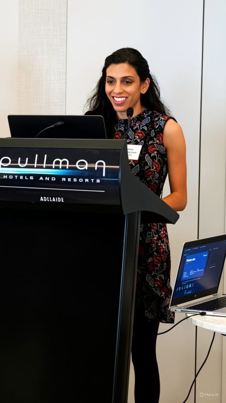 A woman stands at a lectern, mid-speech